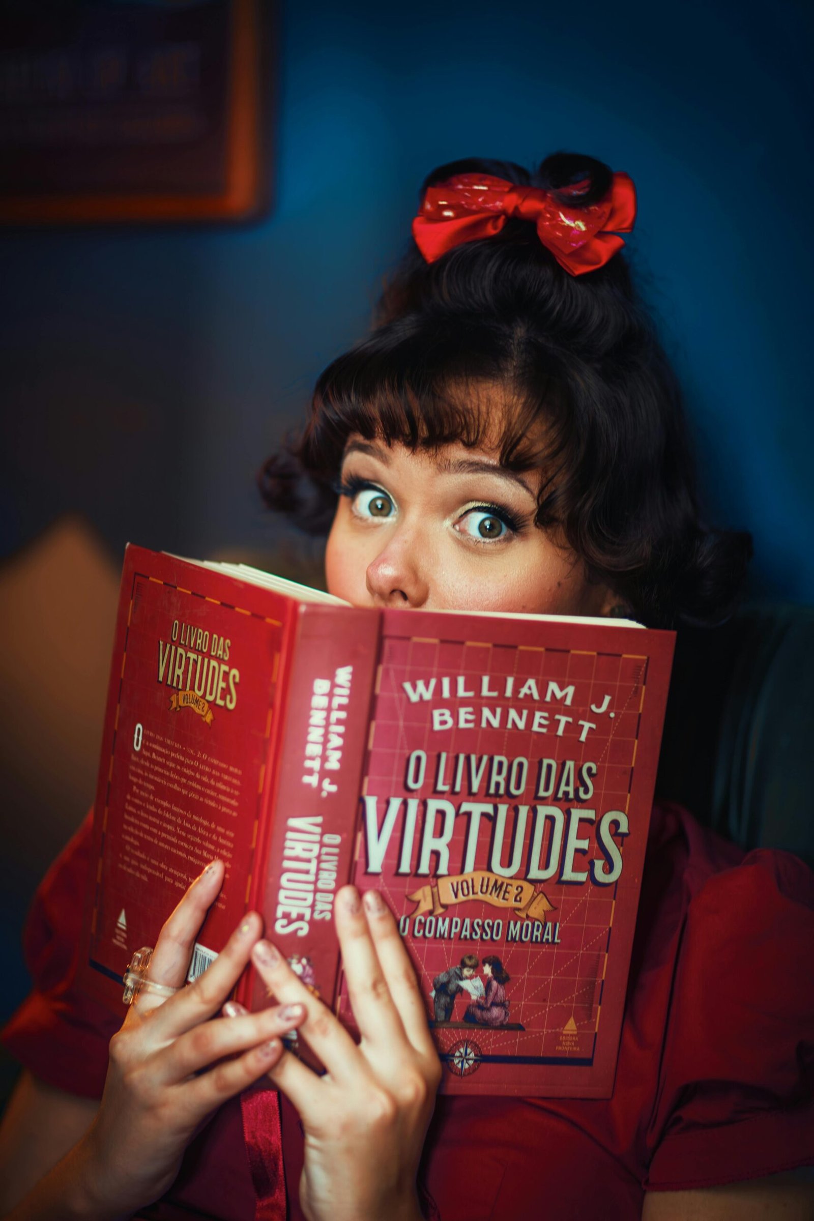 Stylish woman with retro hairstyle reading 'O Livro das Virtudes' indoors.