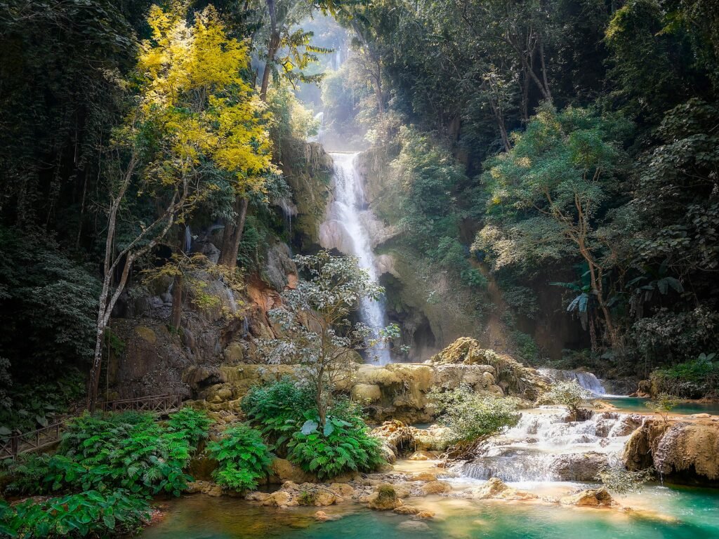 Serene waterfall cascading through dense jungle in Laos, surrounded by vibrant foliage.